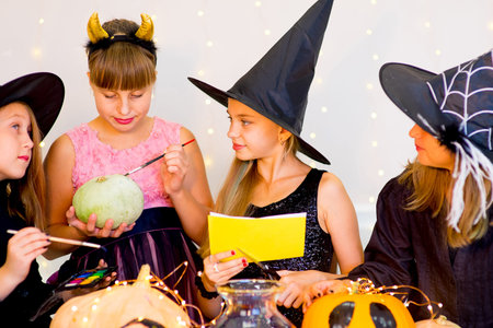 Happy group of teenagers in costumes preparing for Halloween, playing around the table with pumpkins and bottle of potionの写真素材