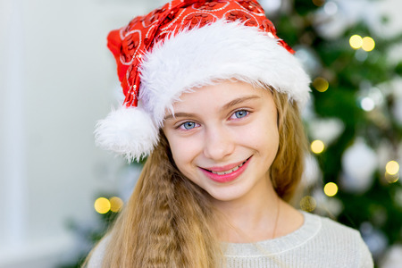 portrait of a girl with a Christmas hat near Christmas tree in the white roomの写真素材