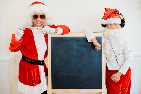 two boys pretending he is a Bad Santa with chains, headphones and sunglasses, near black boardの写真素材