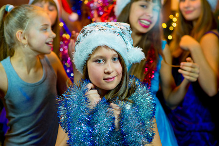 Group of cheerful young girls celebrating Christmas near the Christmas tree with lights. Disco. First planの写真素材
