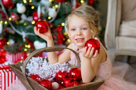 little girl looks at Christmas decorations sitting under the Christmas tree near a sofa, a nice smileの写真素材