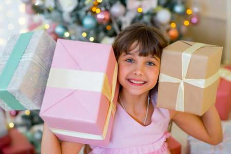 Adorable blonde girl in a pink dress sitting on the bed between Christmas giftsの写真素材
