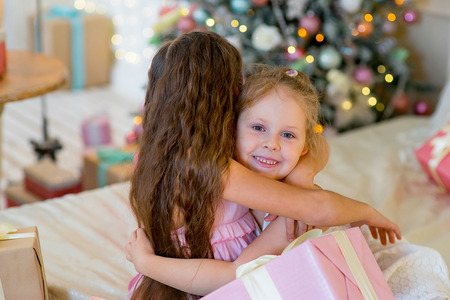 Two young girls give each other gifts in dresses on the bed hugs between Christmas giftsの写真素材
