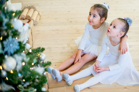 Two young ballet dancer sitting near Christmas tree on the wooden floor and smileの写真素材
