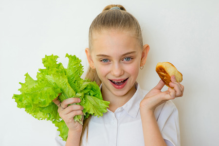 Young girl chooses between a lettuce and baking isolatedの写真素材