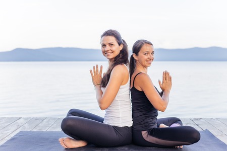 Young attractive smiling women practicing yoga on a lakeの写真素材