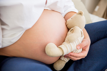 pregnant woman with teddy bear sitting on a bedの写真素材