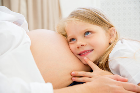 happy smiling pregnant mother hugging with her daughter at homeの写真素材