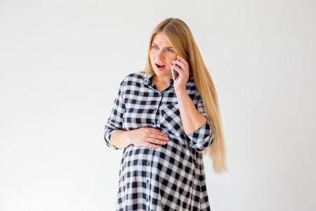 Pregnant woman talking on a mobile phone at homeの写真素材