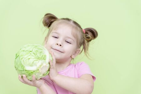little girl 4 years old in a pink T-shirt on a green background holding a swing of cabbage in his hands and smiling. proper nutrition for preschoolersの写真素材