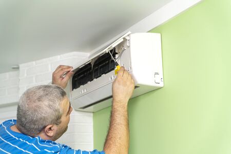 Male technician - repair and diagnostics of air conditioners. Opening the cover and removing the display for repairの写真素材