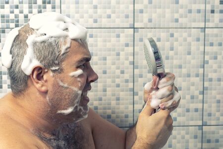 the man in the foam is standing in the bathtub all in the foam and emotionally shakes the shower, there is no water. water failureの写真素材