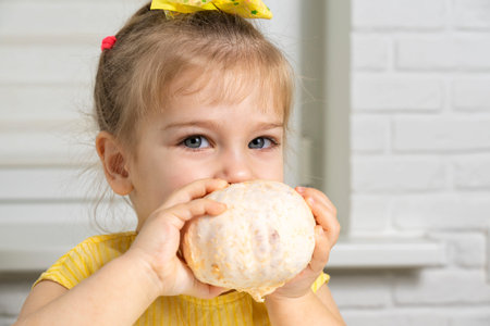 a little girl in a yellow blouse sits at a table in the kitchen, smiles a peeled grapefruit in her...