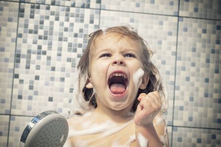 a child of 4 years old is covered in foam in a bathtub in his hand, holds a shower and screams emotionally, there is no water. the child can not wash off the soap, water pipe breakage.の写真素材