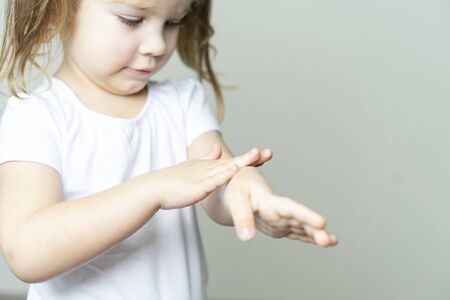 little girl 4 years old in a white T-shirt rubs the sanitizer on her hands. hand treatment in the conditions of the emulsion of coronavirus KOVID-19の写真素材