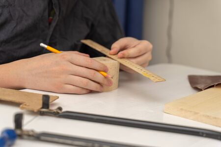 a teenager in a work coat sits at a desk draws a drawing on a box for cutting wood. activities at home during the period of quarantine and self-isolationの写真素材
