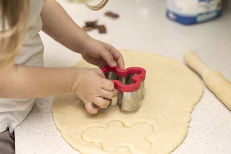 a little girl 3-5 years old cuts out cookies from the dough with a cookie cutter. activities with children in quarantine and self-isolationの写真素材