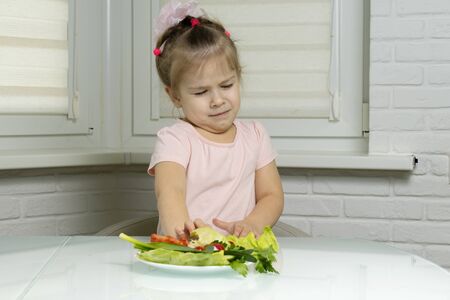 girl preschooler in disgust looks at a plate with vegetables. the problem of a balanced diet of young childrenの写真素材