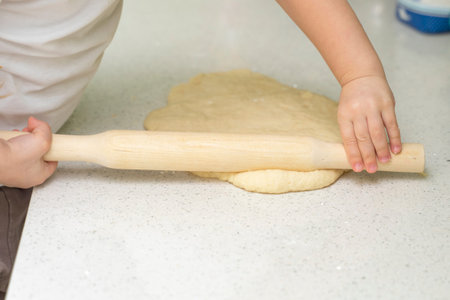 little girl 3-5 years old rolls out the dough with a rolling pin in the kitchen. activities with...