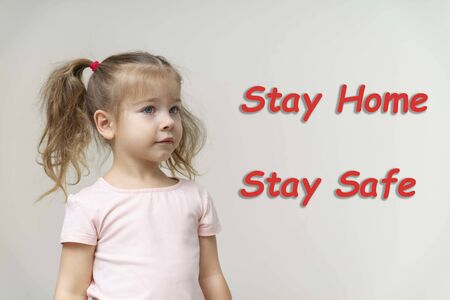 stay home and stay safe save life text on dark background. sitting next to the floor is a little girl in jeans and playing with a wooden airplane. the need to stay home in the midst of a coronavirus pandemicの写真素材