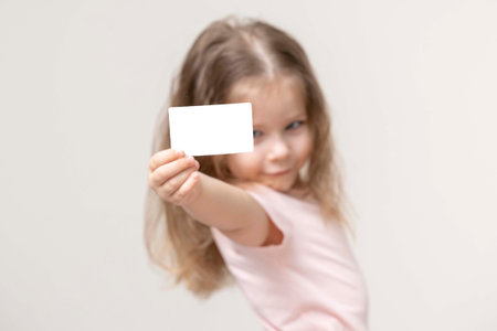 little girl holds a card in front of her and smile, portrait, copy space. advertising space. empty white business cardの写真素材