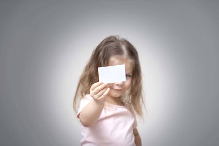 little girl holds a card in front of her and smile, portrait, copy space. advertising space. empty white business cardの写真素材