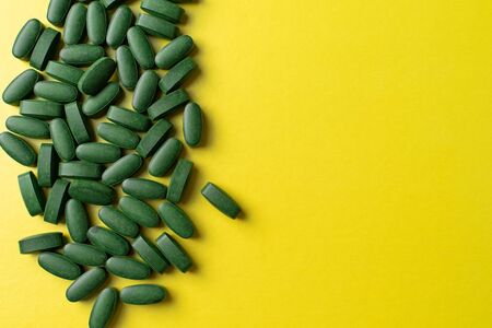 green pills chlorella on a yellow background. nutritional supplements for a healthy dietの写真素材