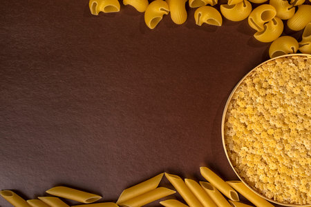 wooden round cup with stelline, pepe rigate, snails and penne, feathers. set of italian pasta on a brown background with copy spaceの写真素材