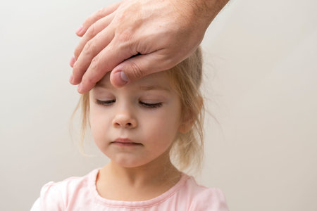 the manâ€™s hand lies on the forehead of a three-year-old girl. Dad checks the temperature of...