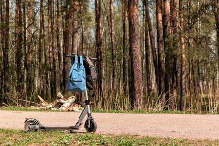 on a spring forest path there is an electric scooter, two backpacks hang on it
