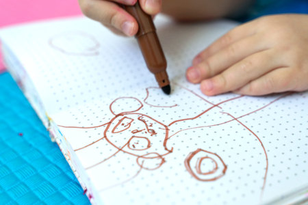 girl draws with felt-tip pens on a colored background. brown drawing on a white sheet. children's...