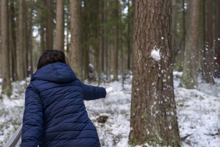 woman throws a snowball at a tree. the snowball is breaking on a tree. winter funの写真素材