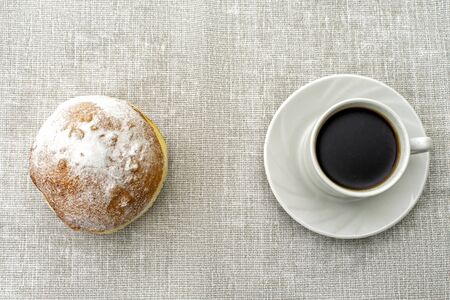 cup of coffee in a white cup and a donut on a light surfaceの写真素材