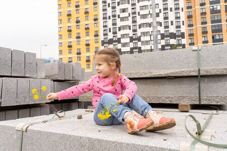 little girl plays on a pile of building blocks against the background of new buildingsの写真素材