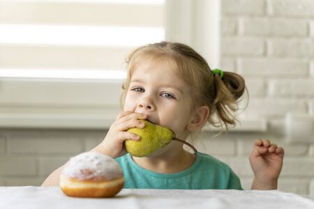 the child picks the pear, not the donut. proper nutrition concept. right choice. fruits instead of sweetsの写真素材