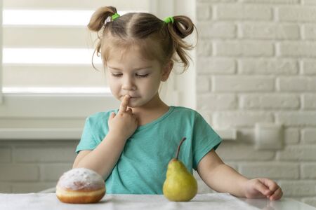 little girl chooses between donut and fruit. the concept of proper nutrition, the right choiceの写真素材