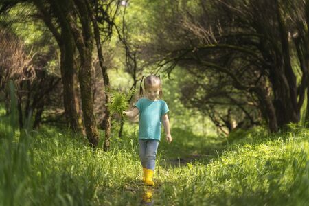 Little girl walks through puddles in rubber boots in the woodsの写真素材