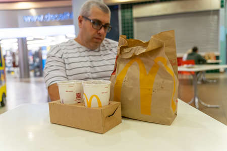 07 19 2020 Russia, Moscow.a man sits at a table in a McDonalds restaurant, in front of him is an individually wrapped food bag. rejection of common trays in restaurants due to the coronavirus.のeditorial素材
