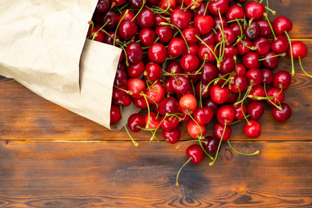 ripe juicy cherries in a paper bag on a wooden table, selective focus