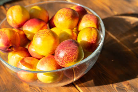 ripe juicy nectarines in a glass bowl on a wooden table on a sunny dayの写真素材