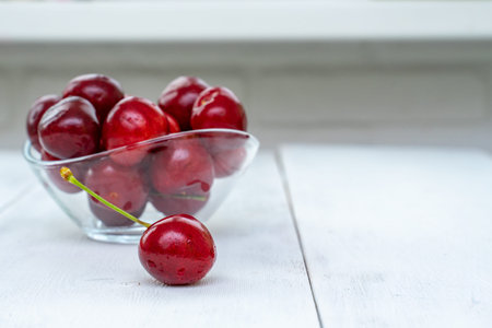 A heap and a large glass bowl of fresh red ripe cherries on a white wooden background
