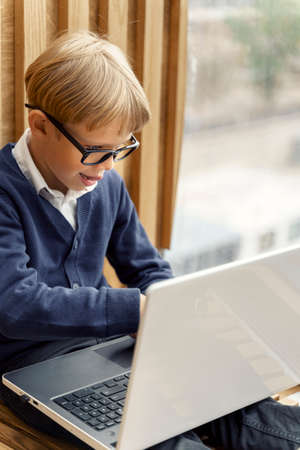 little boy in glasses and business clothes works on a white laptopの写真素材