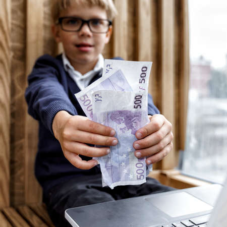 the boy sits at the computer and shows money to the camera. online shopping by childrenの写真素材