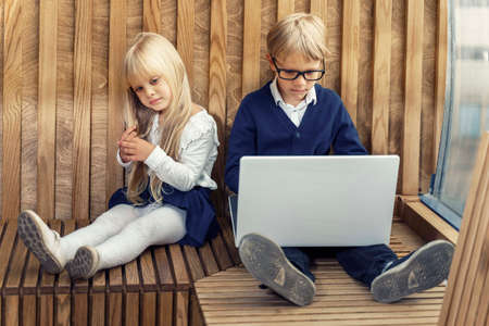 two children with a laptop. the boy is enthusiastically playing the online game. the girl turned away resentfully. gadget addiction problem in children.の写真素材