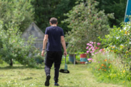 blurry picture out of focus. a man walks with an electric mower in his hands through the village, rear viewの写真素材