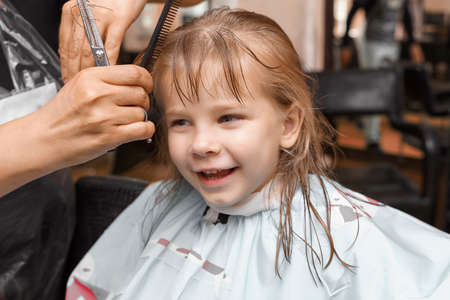 beautiful little red-haired girl at the barber shop. A girl is given the length of her hair in a beauty salon.の写真素材