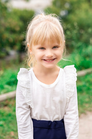 beautiful little blonde girl in white blouse smiling outdoors