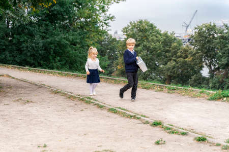 boy and girl are walking along the road. the boy helps the girl carry the briefcase. children's romantic walk.の写真素材