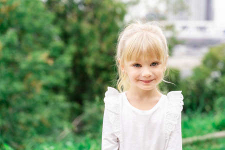 beautiful little blonde girl in white blouse smiling outdoors. copy space to the leftの写真素材