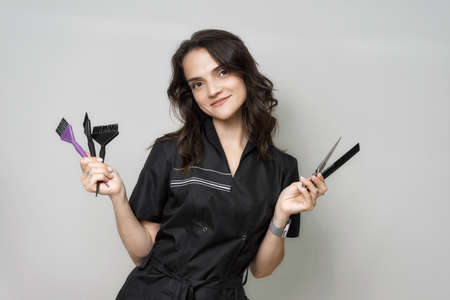 young woman hairdresser in a black work gown holds scissors and brushesの写真素材